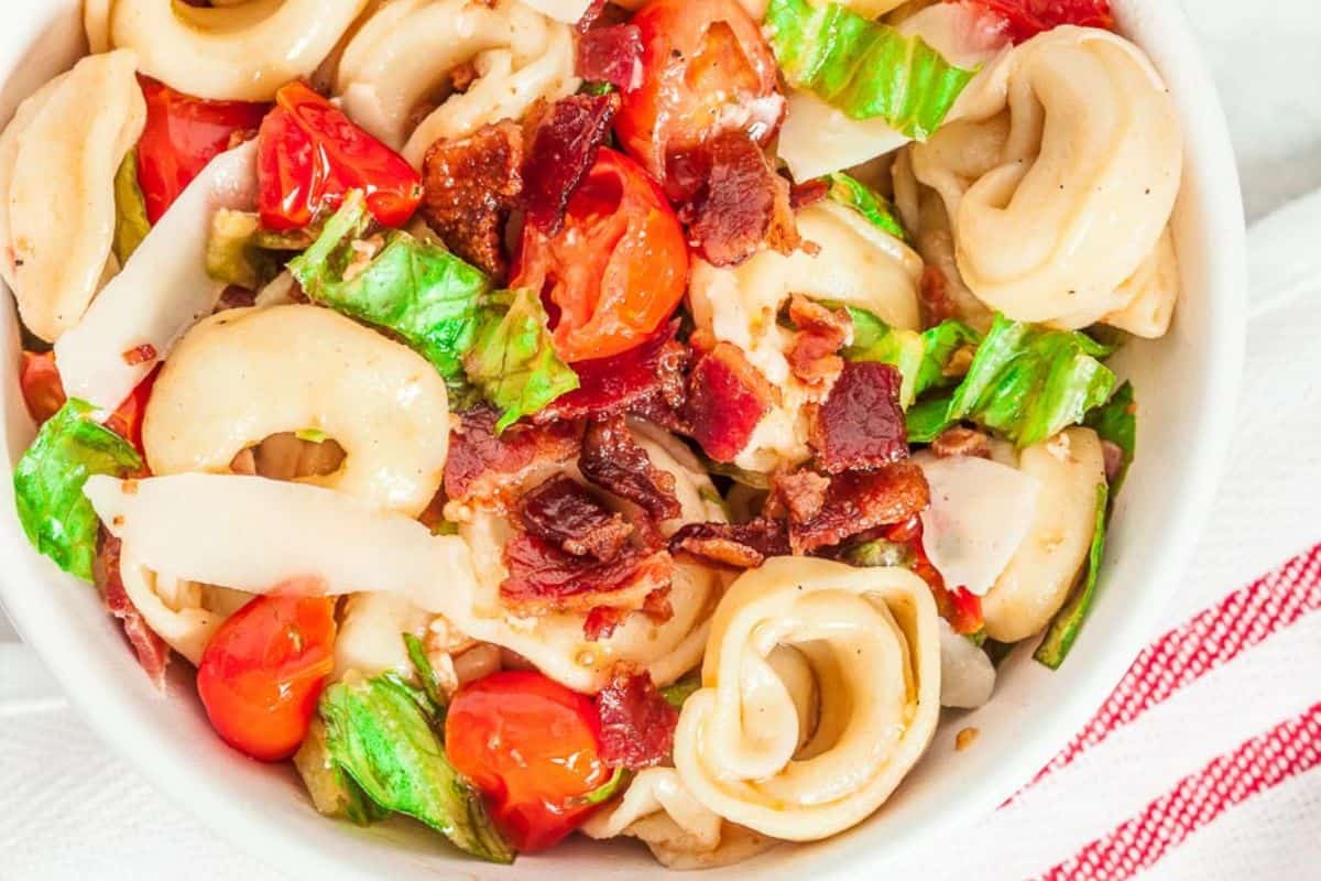 Tortellini pasta in a bowl with bacon, lettuce, and chopped tomatoes.