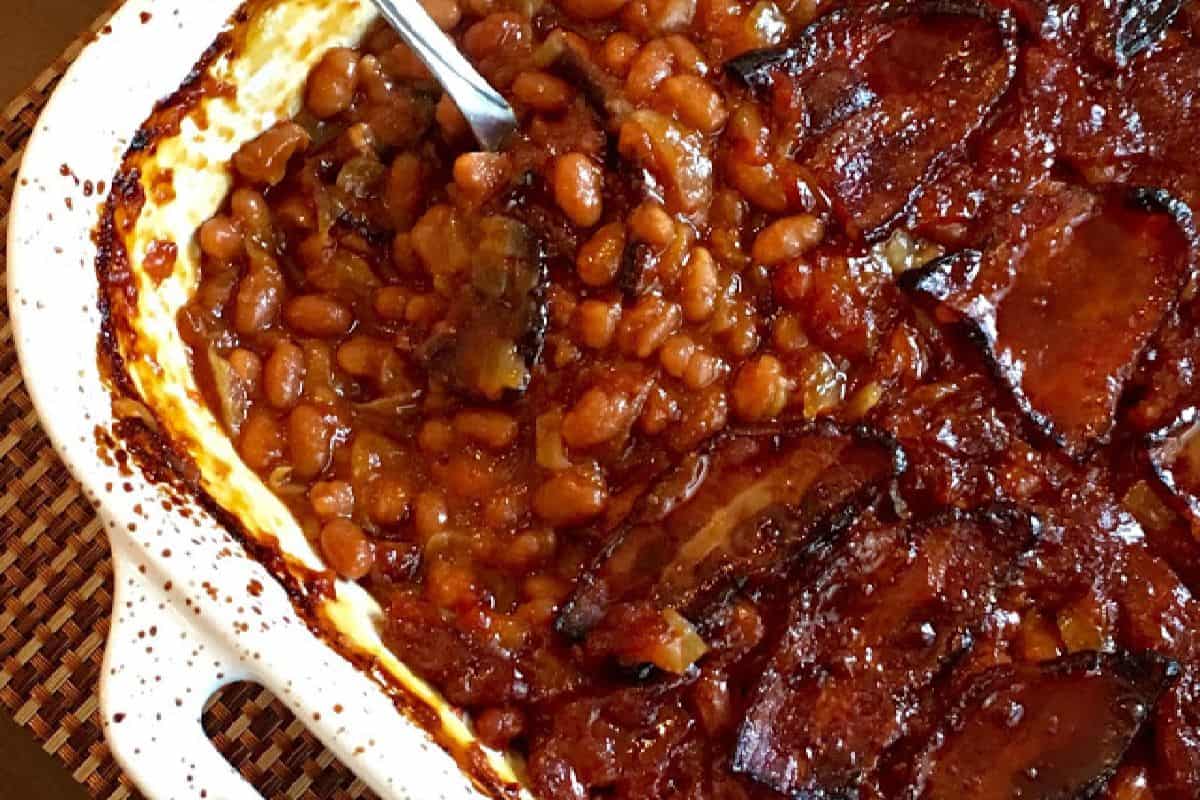 The image depicts a baked dish of beans in a savory sauce, topped with slices of browned bacon.