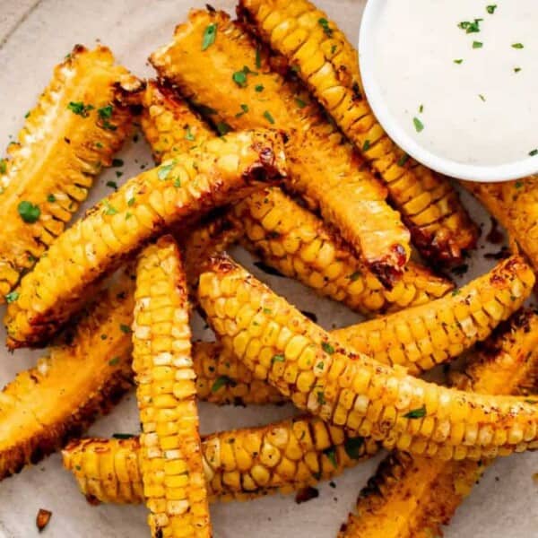 A plate of grilled corn ribs next to a small bowl of dipping sauce.