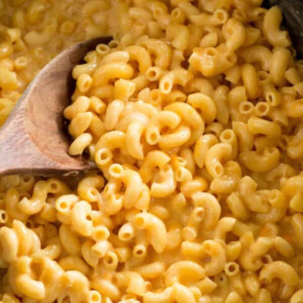 A wooden spoon stirring creamy macaroni and cheese in a slow cooker.