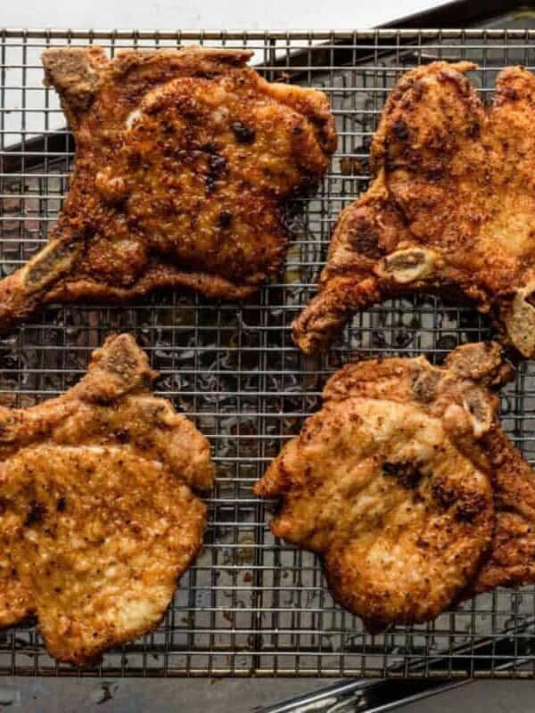 Four seasoned, cooked pork chops on a wire rack set over a baking sheet.