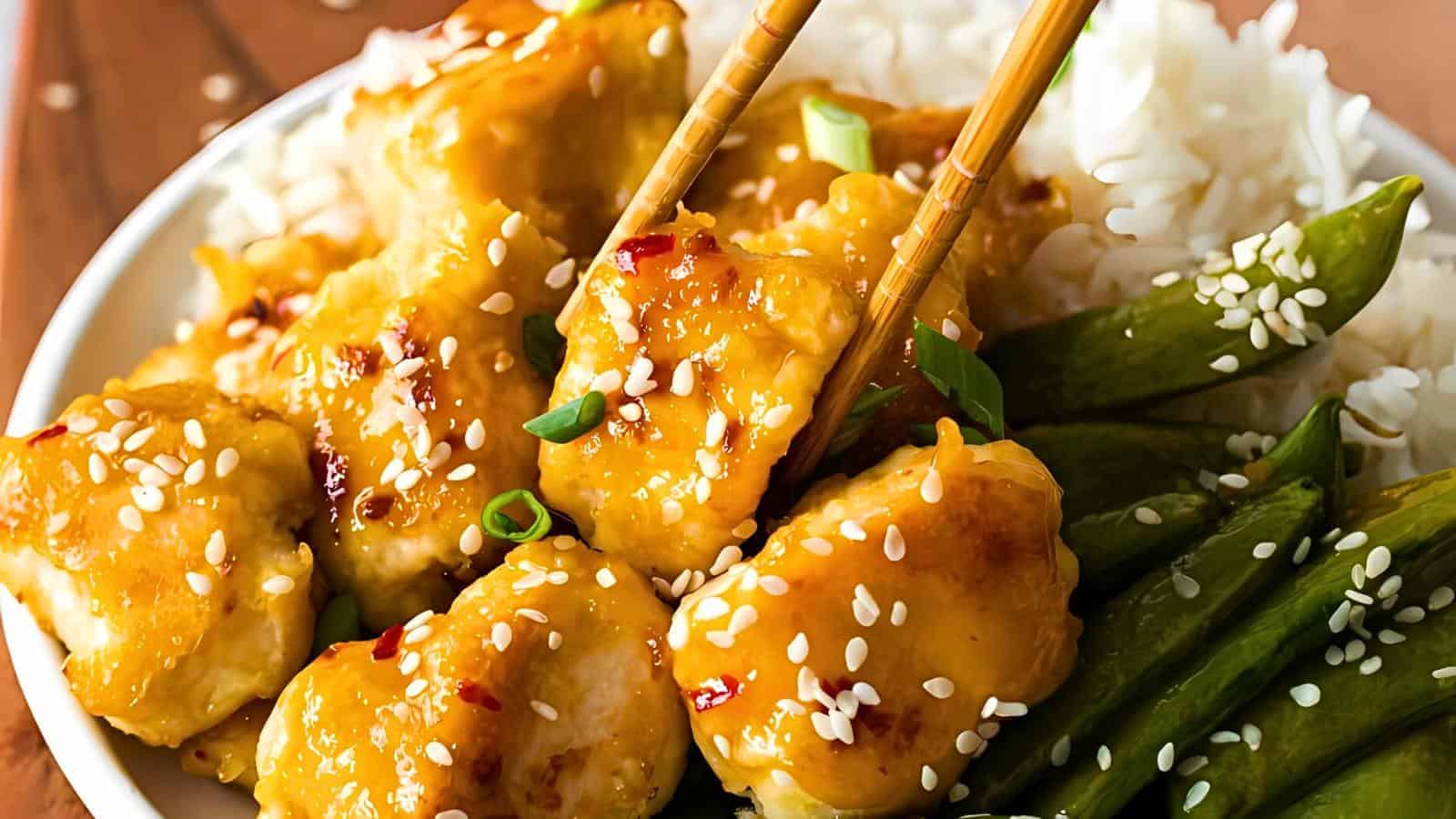 White rice, green beans, golden glazed chicken pieces with sesame seeds and green onions, chopsticks holding a piece of chicken.