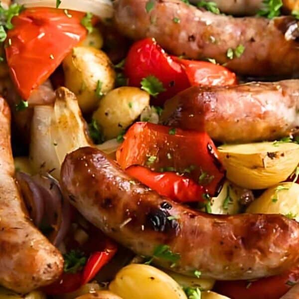 Roasted sausages, baby potatoes, red onions, and red bell peppers with chopped parsley on a baking tray.