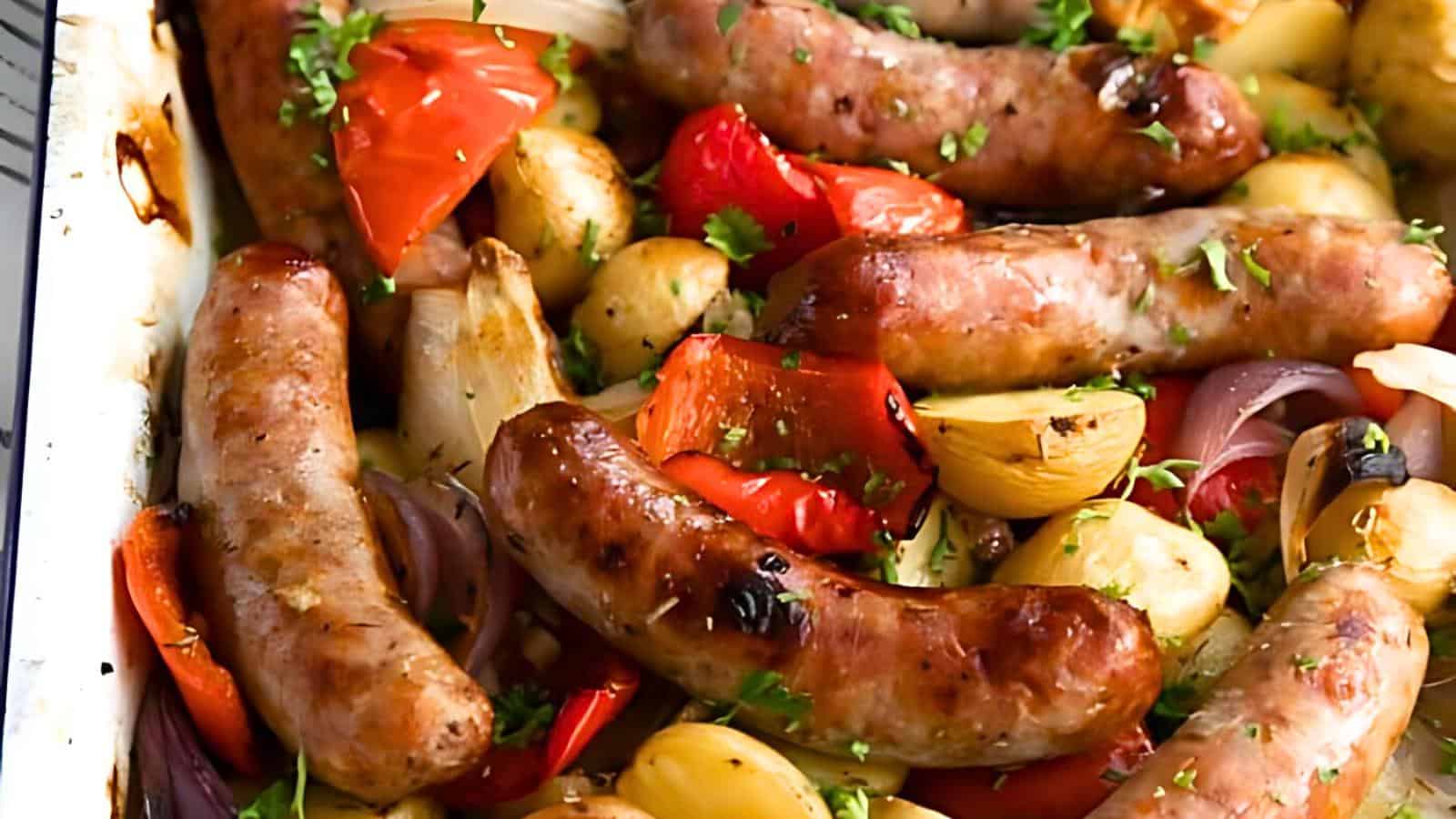 Roasted sausages, baby potatoes, red onions, and red bell peppers with chopped parsley on a baking tray.