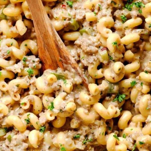 A close-up of creamy macaroni pasta with ground beef and chopped green peppers, garnished with parsley and stirred with a wooden spoon.