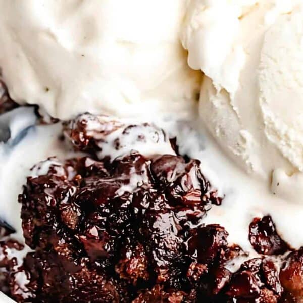 A bowl with chocolate dessert, two melting scoops of vanilla ice cream, and a spoon scooping some of the dessert.