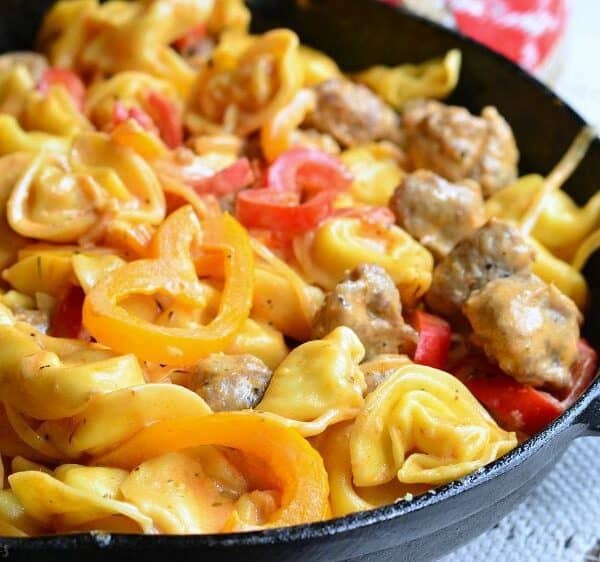 Cheese tortellini, sausage pieces, and sliced yellow and red bell peppers in a cast iron skillet.