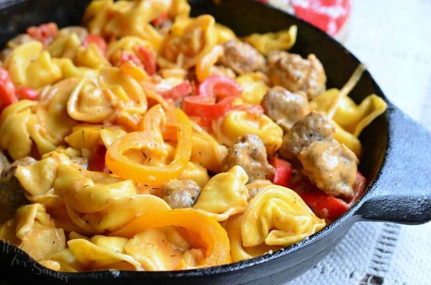 Cheese tortellini, sausage pieces, and sliced yellow and red bell peppers in a cast iron skillet.