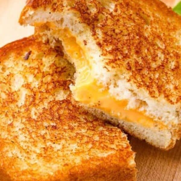 A grilled cheese sandwich cut in half, showing melted cheese between golden brown toasted bread slices on a wooden surface.