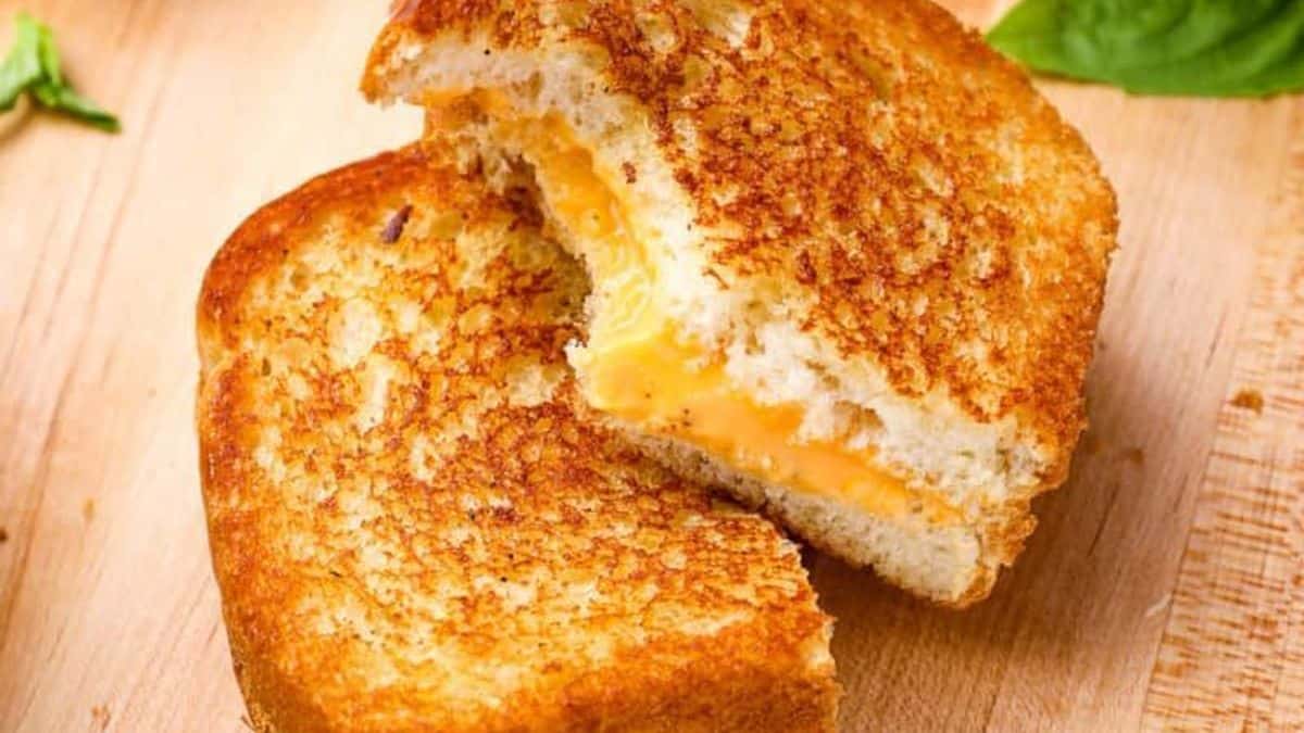 A grilled cheese sandwich cut in half, showing melted cheese between golden brown toasted bread slices on a wooden surface.