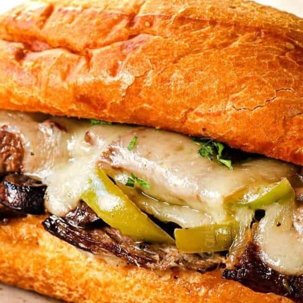 A close-up of a sandwich with melted cheese, grilled beef, and green bell peppers in a toasted hoagie roll.