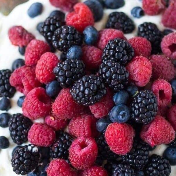A tart filled with whipped cream and topped with fresh raspberries, blackberries, and blueberries.