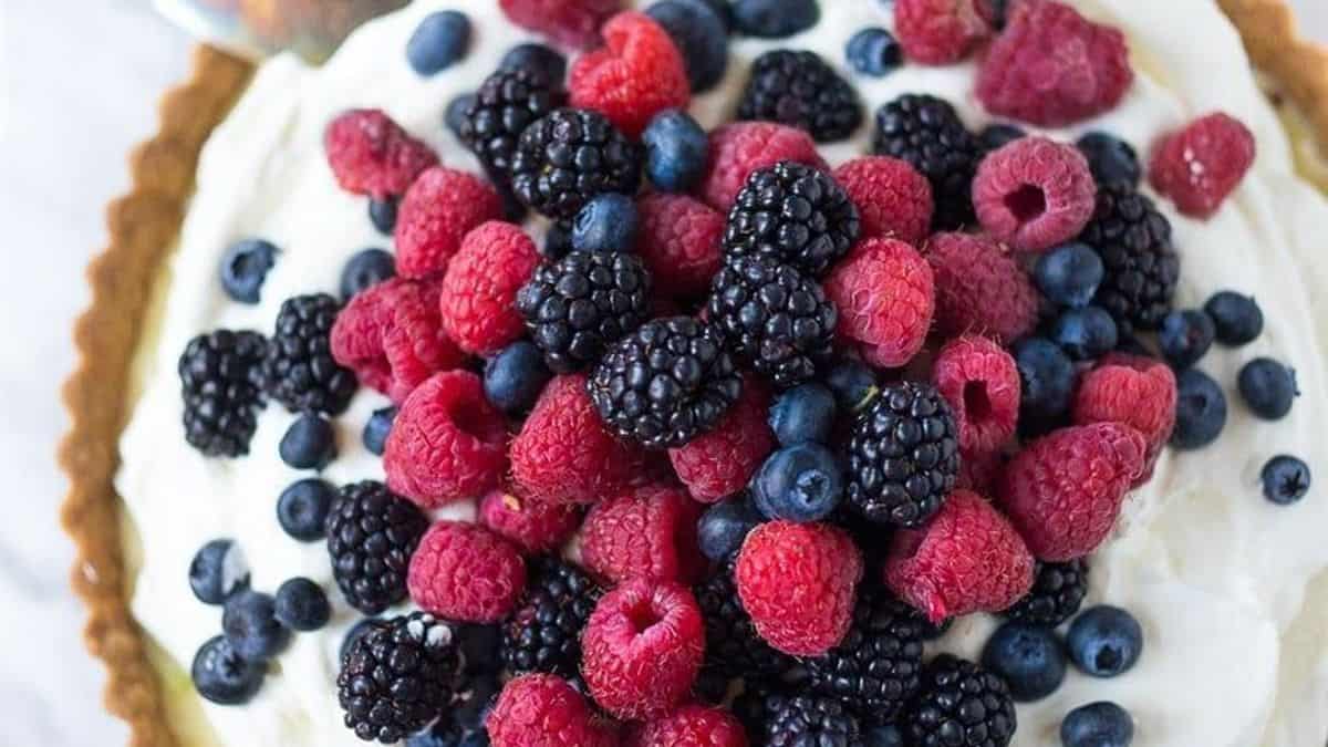 A tart filled with whipped cream and topped with fresh raspberries, blackberries, and blueberries.
