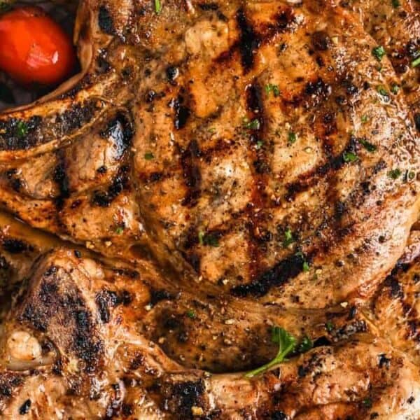 Grilled pork chops with char marks, accompanied by cherry tomatoes and chopped zucchini.