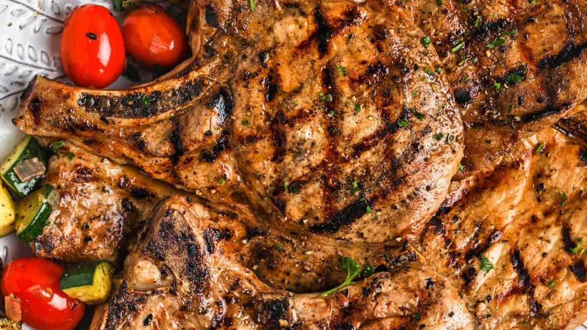 Grilled pork chops with char marks, accompanied by cherry tomatoes and chopped zucchini.