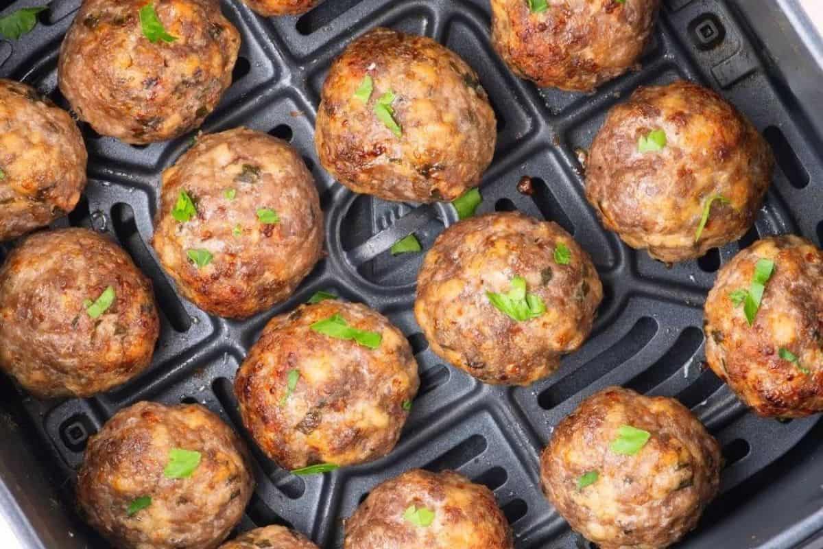 Golden-brown meatballs garnished with fresh parsley are arranged in the basket of an air fryer. The meatballs are evenly spaced and appear perfectly cooked with a slightly crispy exterior.
