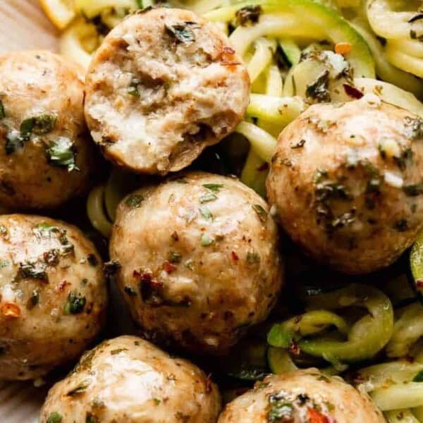 A plate featuring seasoned meatballs and spiralized zucchini noodles, with one meatball showcasing a bite taken out.