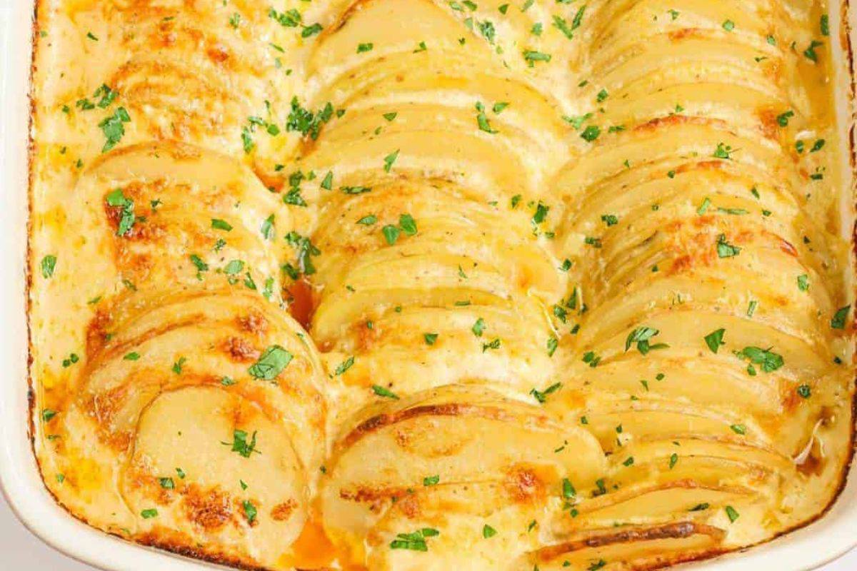 A baked dish of scalloped potatoes arranged in neat overlapping layers, with a golden brown top and garnished with chopped parsley. The creamy sauce is visible between the layers of tender potato slices.