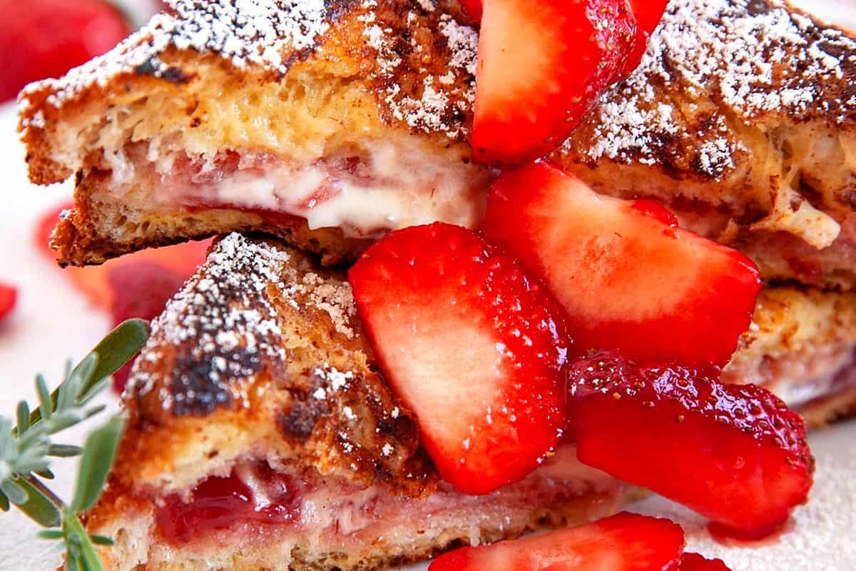 A close-up of French toast stuffed with strawberries, topped with fresh strawberry slices and powdered sugar.