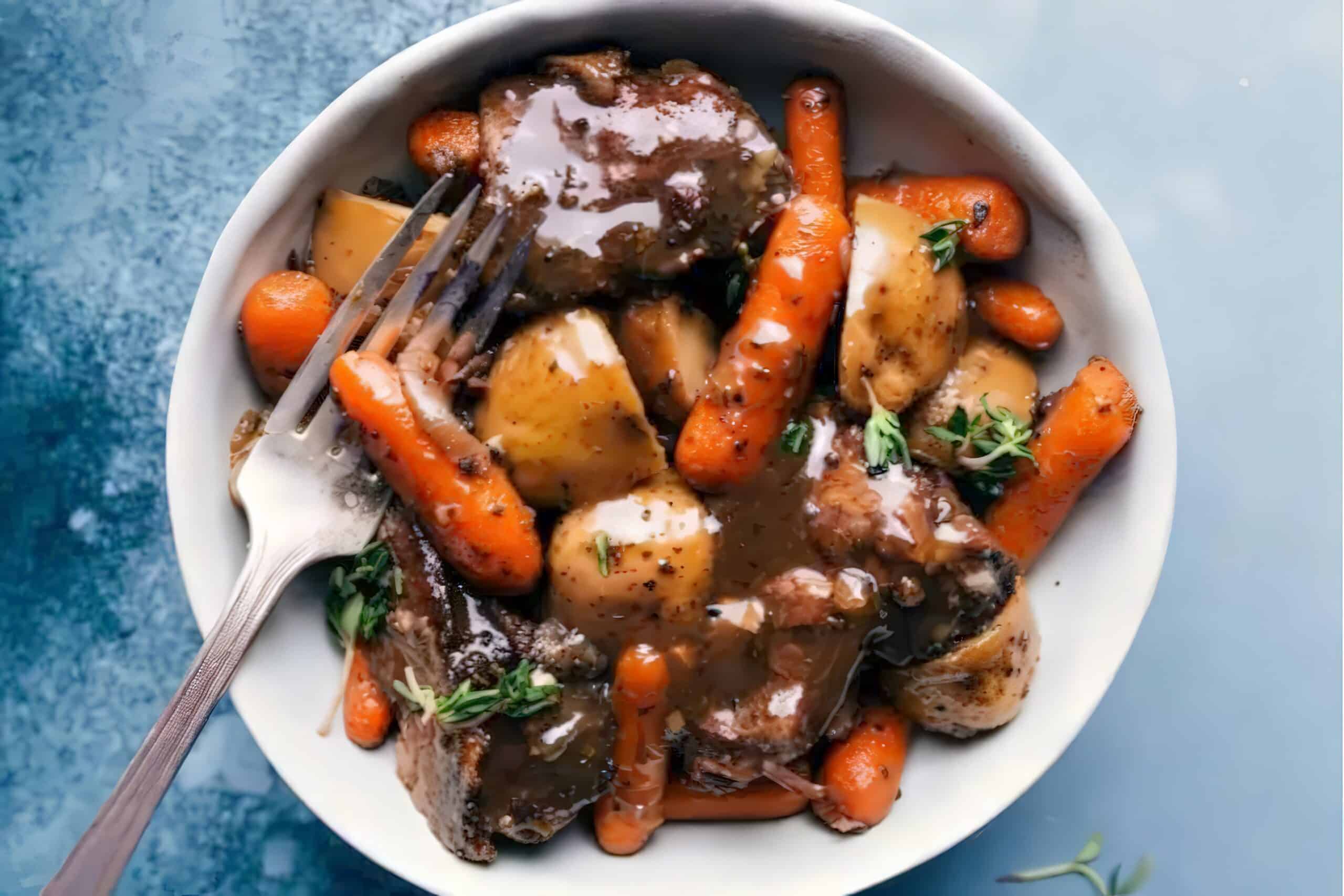 A bowl filled with a savory dish consisting of tender pieces of beef, baby carrots, diced potatoes, and a rich brown sauce, garnished with fresh herbs. A fork rests inside the bowl. The background is a blue, slightly textured surface.