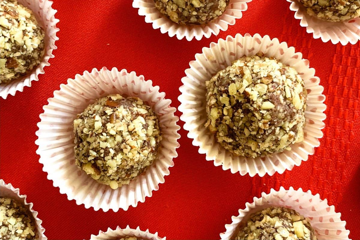 Close-up of several round, nut-covered truffles in white paper cups arranged on a red surface.
