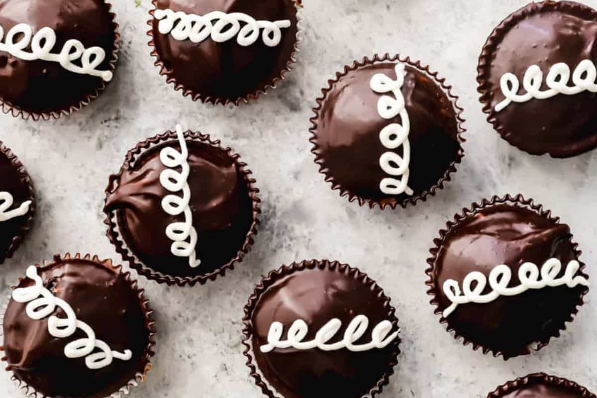 Chocolate cupcakes topped with a swirl of white icing are arranged on a light-colored surface. The cupcakes have a glossy finish and are placed in brown paper liners. The icing on each cupcake is designed with a consistent looping pattern.