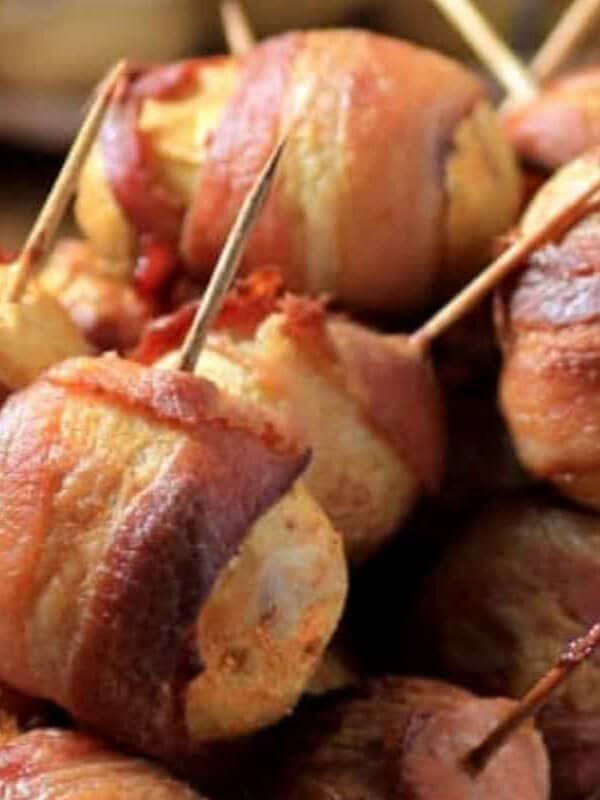 Bacon-wrapped water chestnuts held with toothpicks, arranged on a white plate.