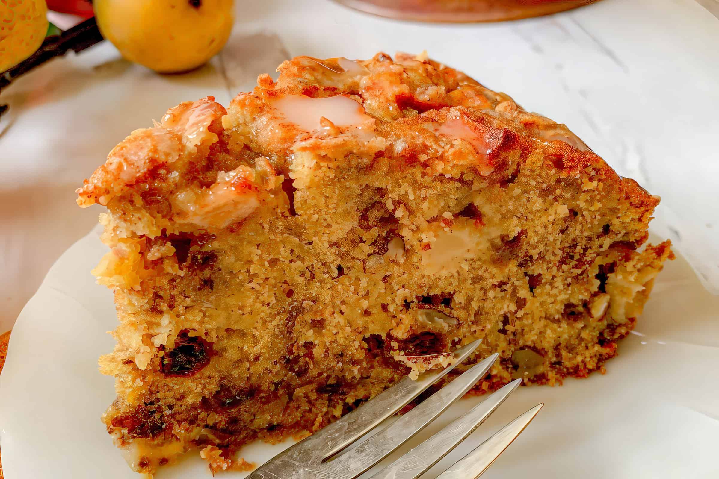 A close-up of a slice of apple bread, featuring a moist texture with visible apple chunks and nuts, on a white plate. A silver fork rests in front of the slice. The background includes an apple, suggesting the ingredients used.