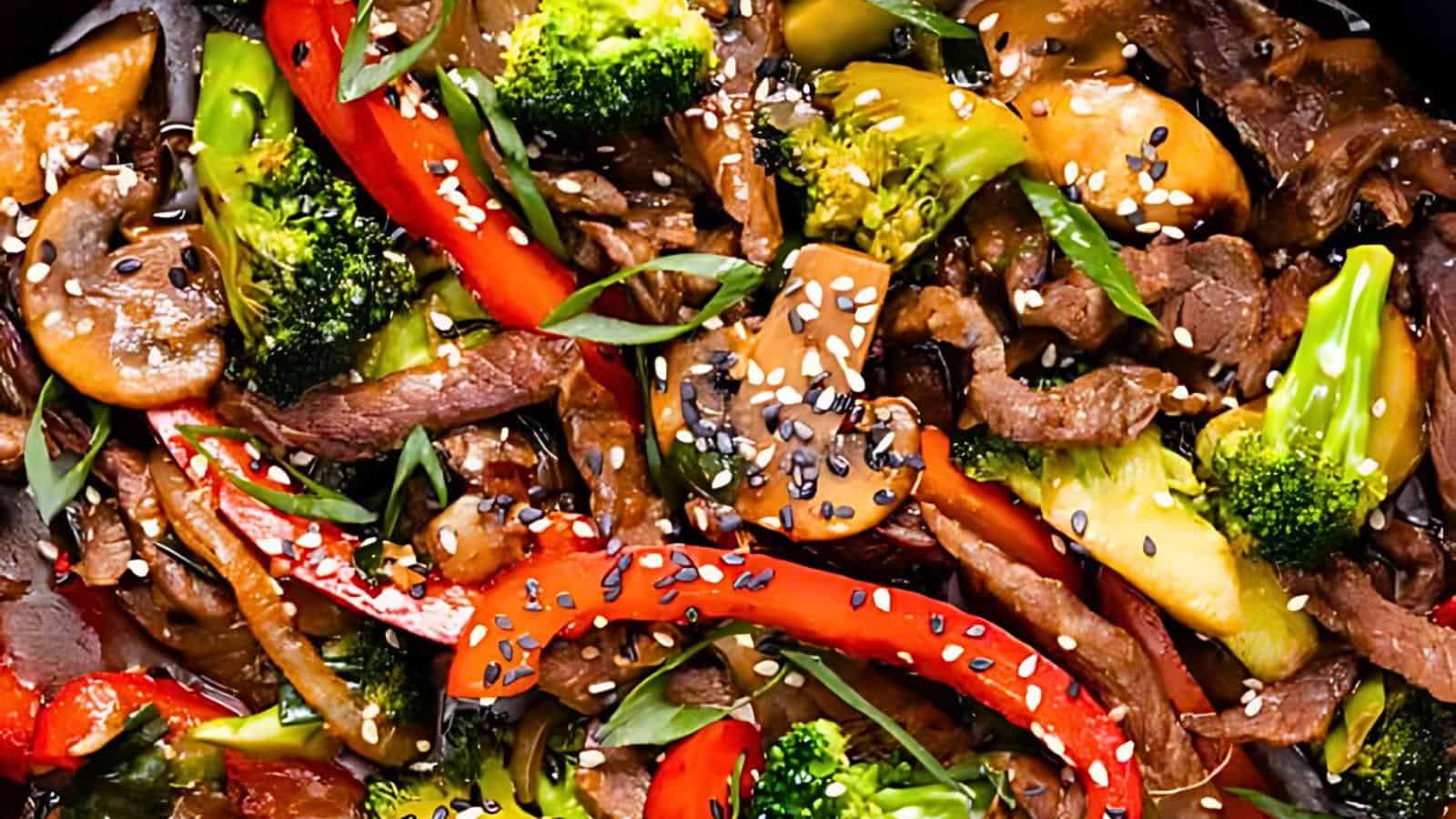 A colorful stir-fry dish with slices of beef, red bell peppers, broccoli florets, mushrooms, and green onions, all topped with sesame seeds. The ingredients are coated in a glossy sauce, making the dish appear vibrant and appetizing.