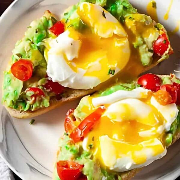 A plate with two pieces of avocado toast topped with cherry tomatoes and poached eggs, alongside a fork.