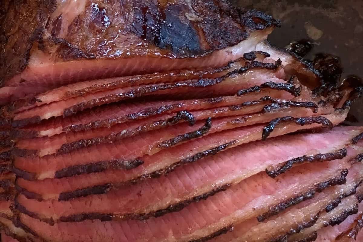 Close-up of honey-glazed, spiral-sliced ham. The meat is tender and juicy, with a rich, caramelized glaze on the edges. The even slices showcase a contrast between the browned exterior and the pinkish interior, highlighting the ham's succulence.
