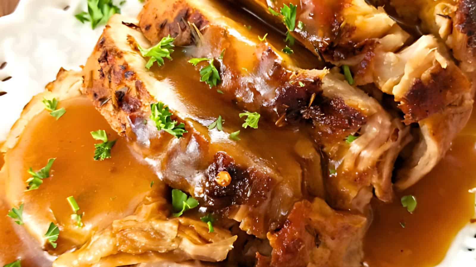 Close-up of a roasted meat dish garnished with fresh parsley and drizzled with rich brown gravy. The meat appears tender and juicy, set on a white plate, with the accompanying herbs adding a touch of color and freshness.