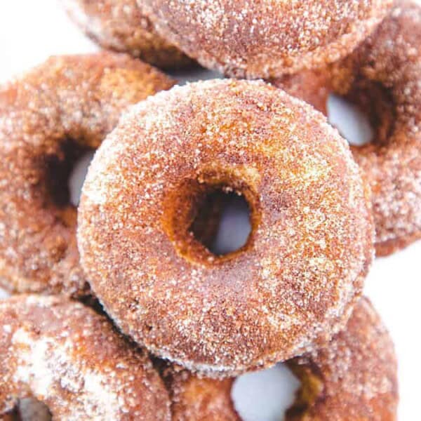 A close-up of several sugar-coated donuts stacked on a white surface.
