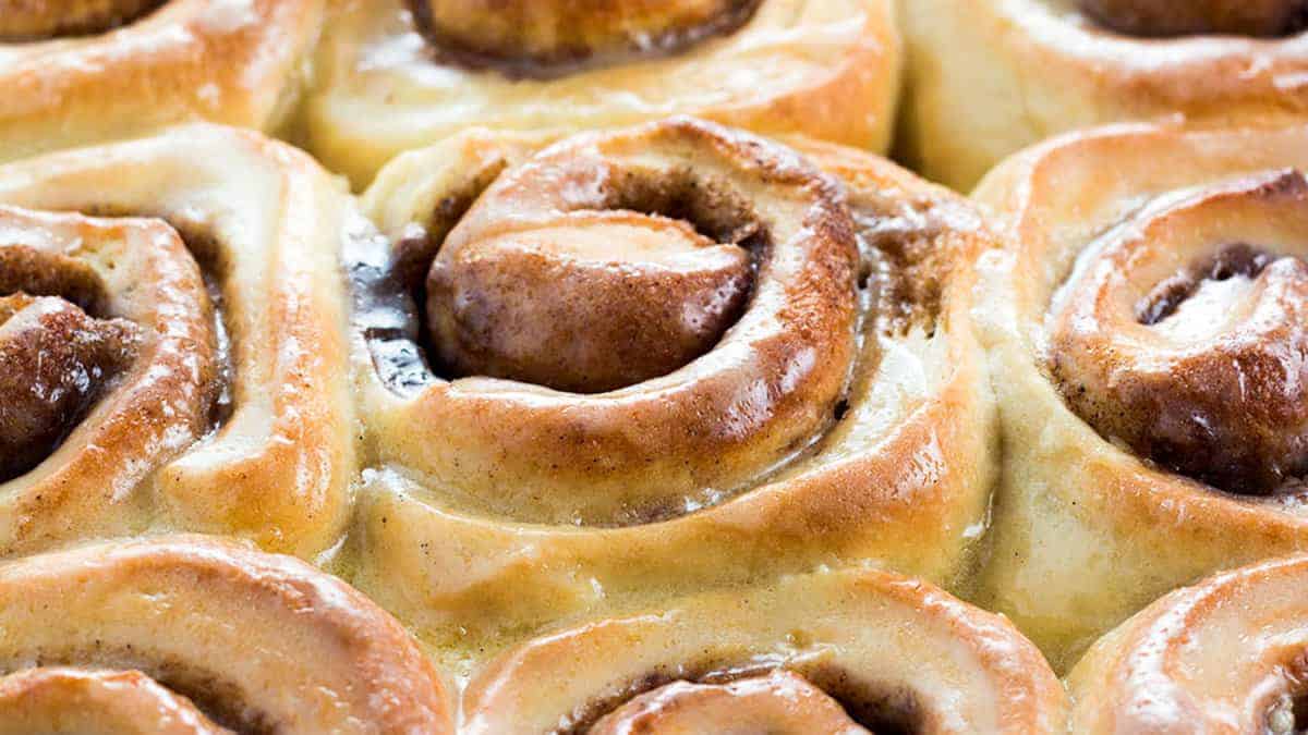Close-up of freshly baked cinnamon rolls with a golden-brown crust and visible swirls of cinnamon filling. The rolls appear soft and glazed, giving them a slightly shiny appearance.