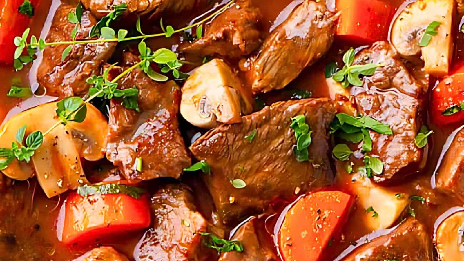A hearty stew with chunks of beef, carrots, and sliced mushrooms garnished with fresh herbs in a rich, savory broth.
