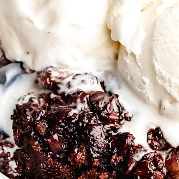 A bowl of chocolate pudding topped with two scoops of vanilla ice cream, with a spoon on the left side.