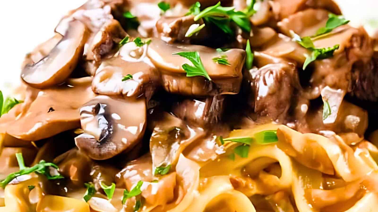 Close-up of a plate of pasta topped with a creamy mushroom sauce. The sauce includes sliced mushrooms, onions, and is garnished with chopped fresh parsley. The dish appears rich and savory, with a smooth texture evident on the pasta and sauce.