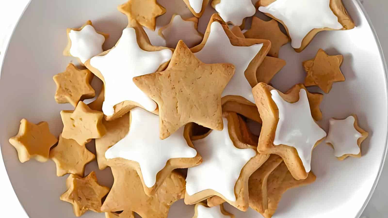 A plate filled with star-shaped cookies. Some cookies are iced in white, and others are plain. The cookies vary in size and are arranged haphazardly, creating a festive and inviting display.