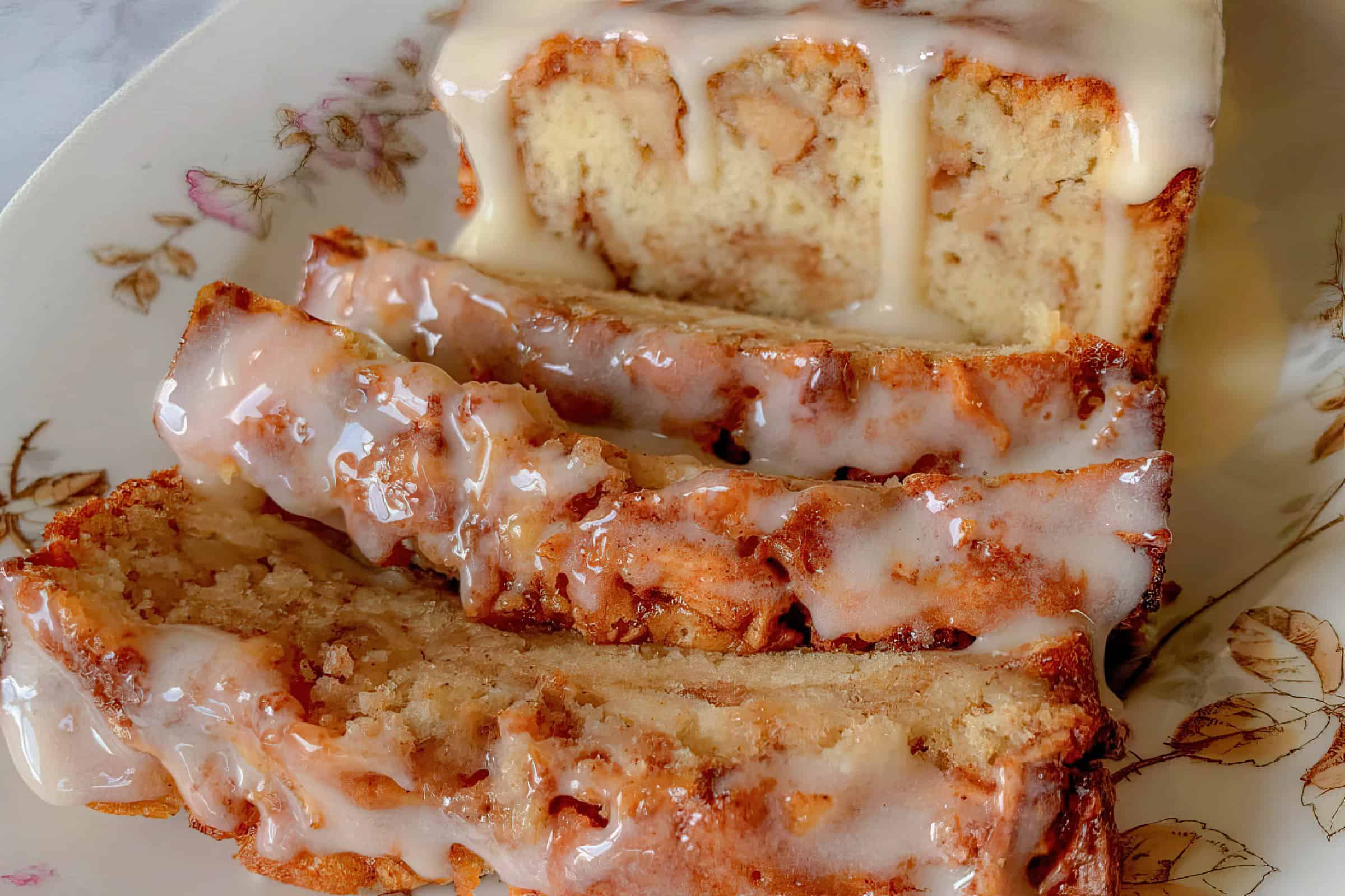 A plate with a charming floral pattern holds four slices of glazed cake. The cake features a light brown crust and thick, creamy icing.