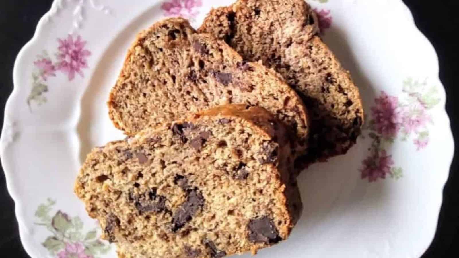 vegan banana bread with chocolate chunks, 3 slices arranges on a white scalloped plate with a delicate pink flower pattern.