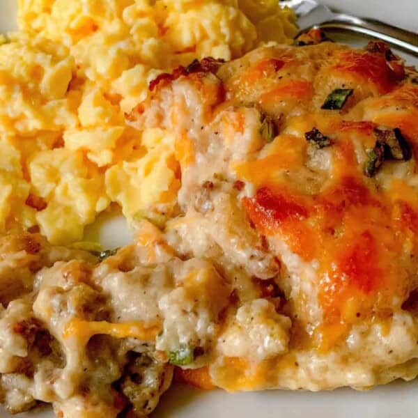 A plate with scrambled eggs and a piece of meatloaf topped with melted cheese and herbs.