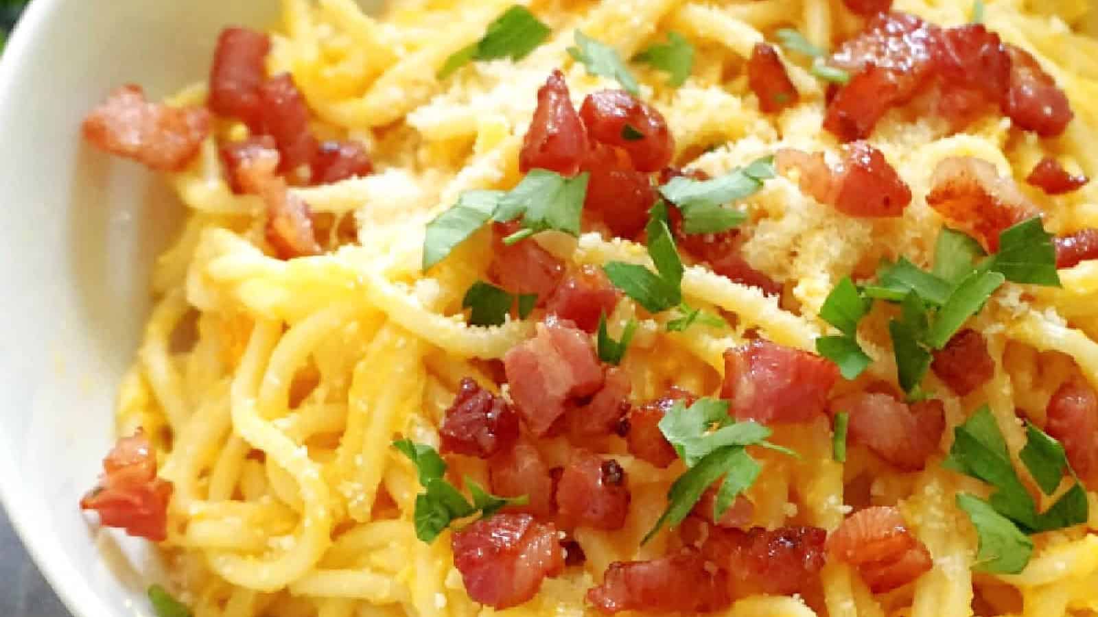 A bowl of spaghetti topped with grated cheese, crispy bacon pieces, and chopped parsley.