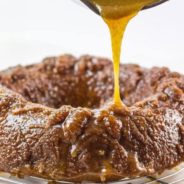 A bundt cake on a wire cooling rack with caramel sauce being poured over the top.