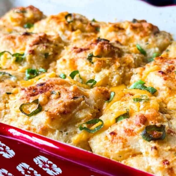 Golden brown cheese biscuits topped with chopped green onions in a red patterned baking dish.
