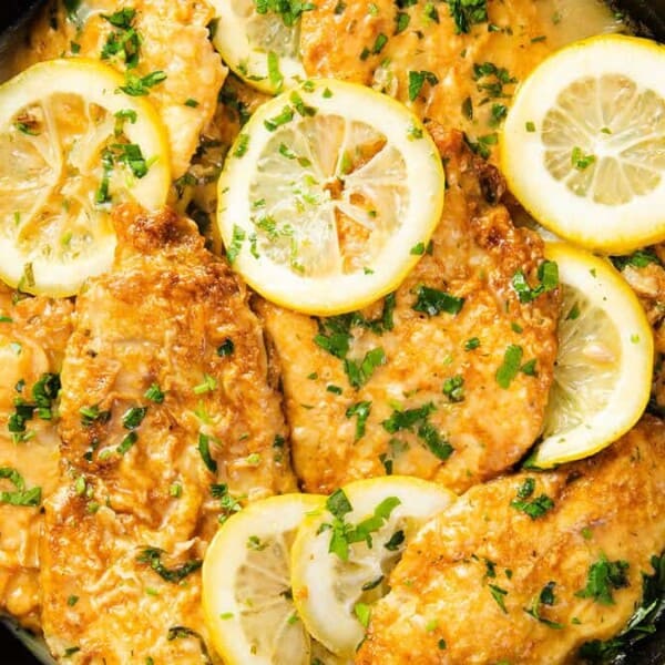 In the image, there is chicken piccata in a skillet with a creamy sauce, garnished with lemon slices and fresh parsley.