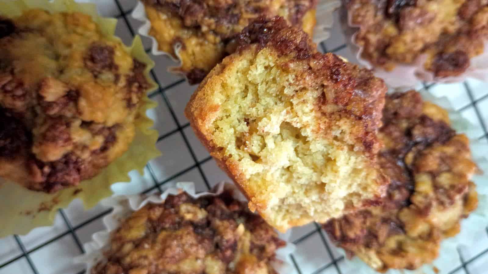 a half of a cinnamon swirl muffin with oatmeal on top of other muffins on a cooling rack.