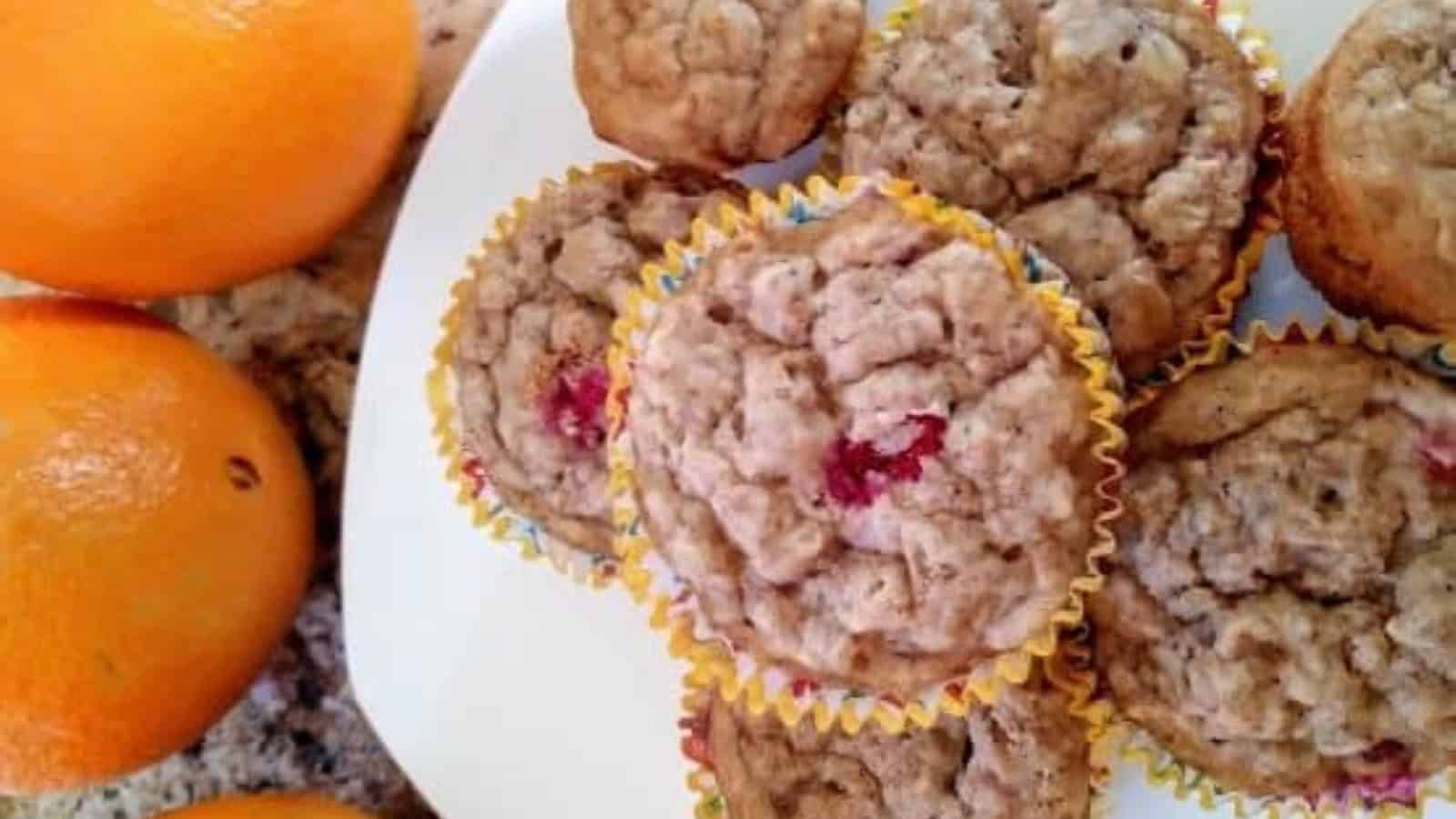 cranberry orange oatmeal muffins in plat with whole oranges next to them.