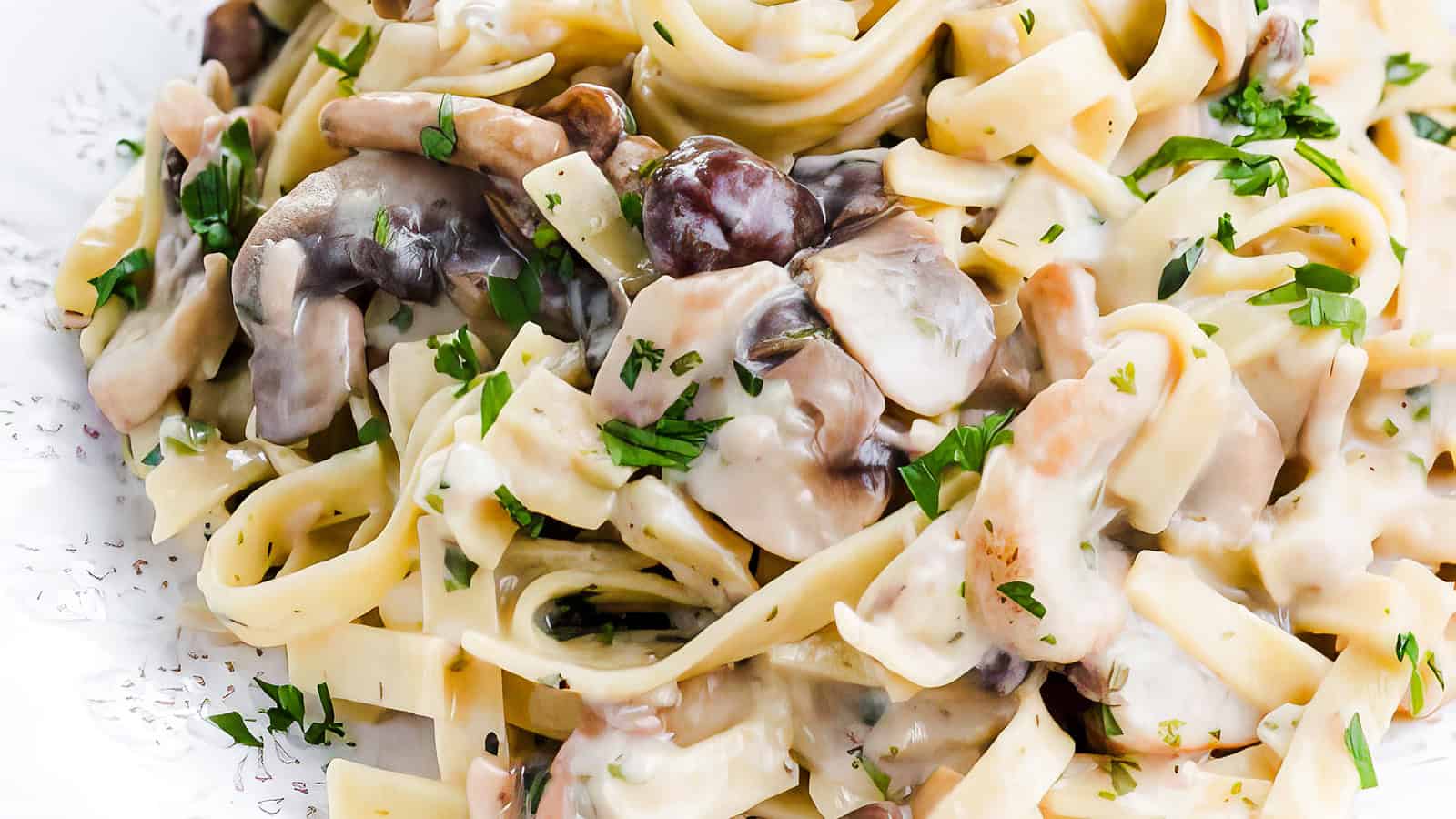 A close-up of creamy mushroom fettuccine garnished with chopped parsley on a white plate.