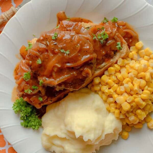 A plate of meatloaf with gravy, served with mashed potatoes and corn on the side, garnished with parsley. The plate is set on an orange-patterned napkin.