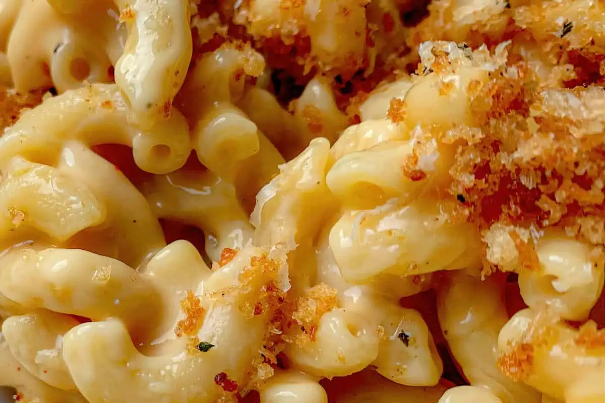 Close-up shot of creamy macaroni and cheese topped with golden brown breadcrumbs. The elbow macaroni is coated in a rich, cheesy sauce, with the breadcrumbs adding a crunchy texture. The dish appears hot and freshly prepared.